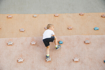 little boy climbing stone wall on playground. sport life concept