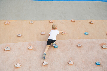 little boy climbing stone wall on playground. sport life concept