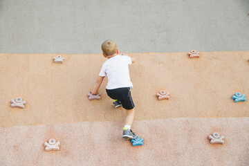 little boy climbing stone wall on playground. sport life concept