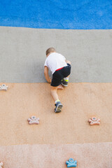 little boy climbing stone wall on playground. sport life concept
