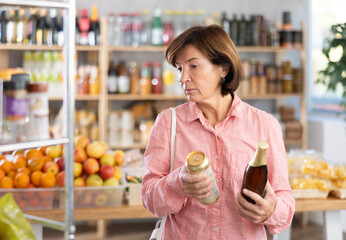 Concerned old woman deciding between kinds of beer in the supermarket