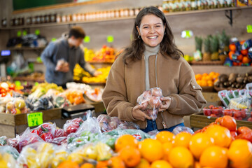 Young woman shopper in casual clothes chooses onions in vegetable shop