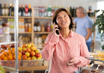 Woman shopper is talking on mobile phone while her husband is shopping in produce section of a supermarket