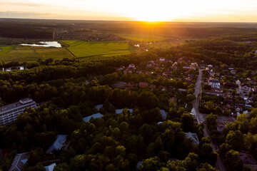 Aerial view of evening suburban landscape, sun shining on rural fields in the distance