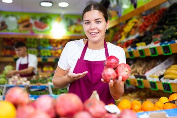 Young saleswoman proposing pomegranate, offering fresh fruits in supermarket
