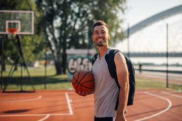 Fototapeta premium Young basketball player smiling while holding basketball on court