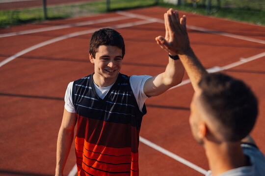 Two basketball players giving high five after game on outdoor court - Powered by Adobe