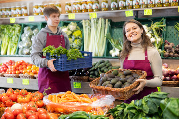 Young woman seller in apron lays out avocados on counter in vegetable shop