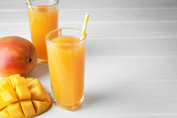 Tasty mango juice in glasses and fresh fruits on white wooden table, closeup. Space for text
