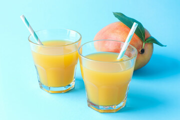 Tasty mango juice in glasses and fresh fruit on light blue background, closeup