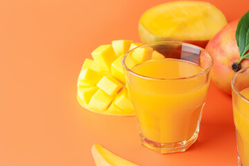 Tasty mango juice in glass and fresh fruits on orange background, closeup. Space for text
