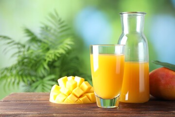 Tasty mango juice in glass, carafe and fresh fruits on wooden table against blurred background,...