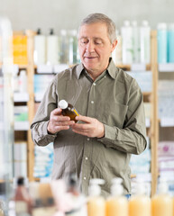 Senior man chooses a medicinal throat syrup in a European pharmacy. Man buys cough and cold syrup