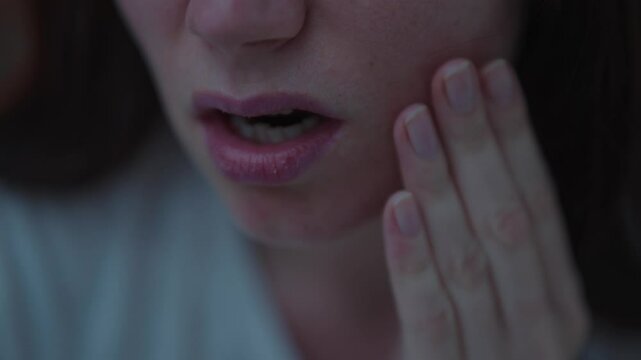 Close-up of a woman suffering from toothache and touching the tooth with her hands in the middle of the night. Concept of nighttime pain in the teeth due to caries