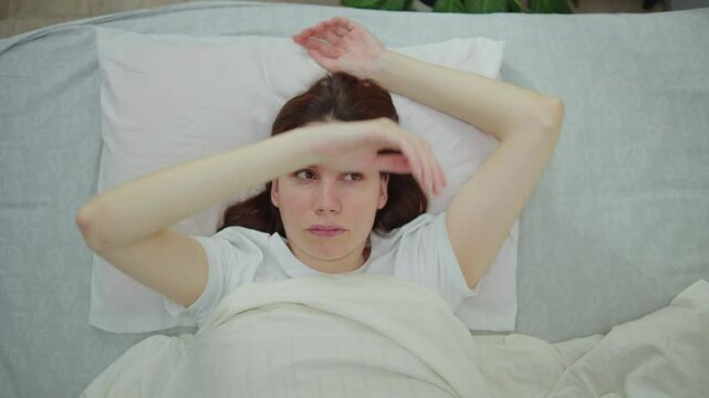 Young adult woman wakes up in the morning in bed and drops her still numb hand after sleeping because of a sleep with an extended arm