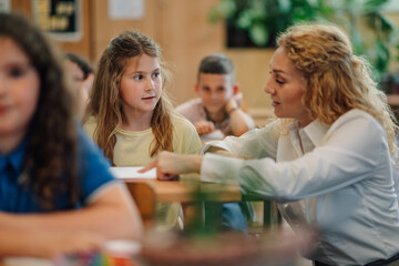 Teacher helping young girl student during class in elementary school