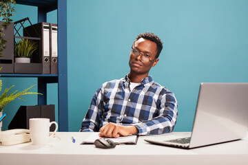 Male finance analyst with crooked glasses, seated at his office desk, feeling tired and stressed...