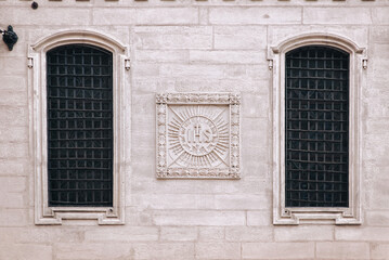 Two antique old windows with black iron bars framed on a light grey wall. The Jesuit Church in Lviv.