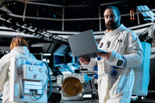 Astronaut reviewing spacecraft diagnostics on laptop to ensure safe operation during long distance space travel. Spaceman uses notebook to monitor system stability during cosmic journey