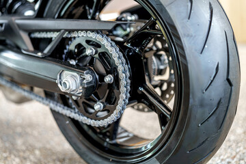 Close-up view of motorcycle rear wheel showcasing chain, sprocket, and tire tread during a warm afternoon