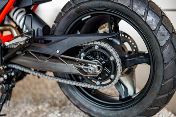 Fototapeta premium Close-up view of a motorcycle rear wheel with chain details in a garage setting during daylight