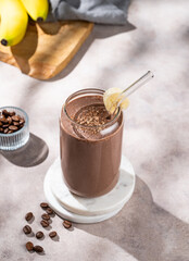 Chocolate coffee smoothie with banana in a glass on a light  background with fruis