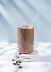 Chocolate coffee smoothie with banana in a glass on a marble stand on a  white blue background