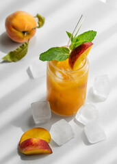 Refreshing peach cocktail, lemonade or iced tea on a white table with shadows, ice cubes and fruits.