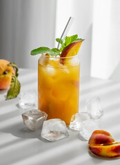 Refreshing peach cocktail, lemonade or iced tea on a white table near window with shadows