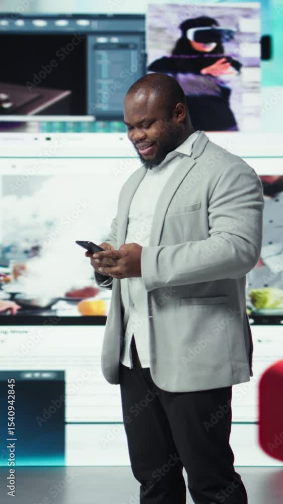 Poster vertical video portrait of smiling man browsing social networks feed on smartphone in front of video