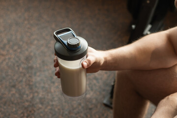 Close up shot of bottle with holding protein shaker in mans hand at gym. Bodybuilder during strength training. Fitness healthy lifestyle concept. Supplement product, creatine, glutamine for workout.