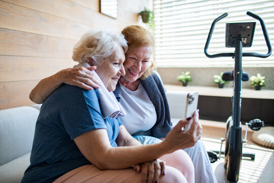 Senior lesbian couple laughing while looking at smartphone after home workout - Powered by Adobe