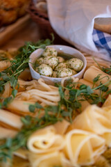 Several types of cheese decorated with young pea shoots and a bowl of mozzarella balls with herb sauce. 
