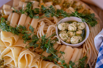 Several types of cheese decorated with young pea shoots and a bowl of mozzarella balls with herb sauce. 
