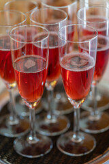 Champagne glasses with a red, gently sparkling beverage standing side by side on a tray. 
