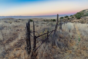 Fototapeta premium A rustic, weathered fence and gate stand in a dry, grassy field in Carrizo Plain National Monument, California, USA. The scene evokes a sense of rural America and the passage of time.
