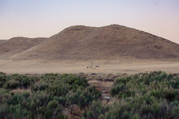 A windmill and shed sit in a field in front of a large hill in the USA. The windmill is used to pump water from the ground for irrigation  Carrizo Plain National Monument, California, USA