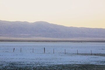 A weathered fence line stretches across the arid landscape of Carrizo Plain National Monument, California, USA. Contrasting with the vast, open playa and distant mountains.