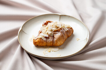 Freshly baked almond croissant rests on a beautiful plate, adorned with delicate almond slices and a dusting of powdered sugar, creating a picturesque dessert display