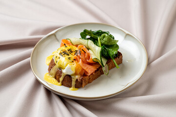 A lavish open-faced sandwich features layers of smoked salmon, a perfectly poached egg, and fresh greens atop rustic bread. This brunch delight shines on an elegant plate surrounded by linen