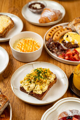 Sharing a vibrant brunch assortment featuring toast topped with scrambled eggs, fresh fruits, baked goods, and creamy desserts surrounded by friends on a sunny morning