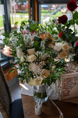 A large wedding bouquet in a vase on the table with white roses and flowers with green leaves, with other gifted bouquets in the background. 
