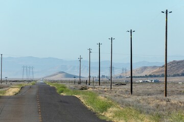 Obraz premium A desolate road stretches through arid landscape in Carrizo Plain National Monument, California, USA. Power lines run alongside, connecting distant towers, symbolizing energy transport.