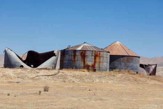 Abandoned and decaying grain silos stand in a field in Carrizo Plain National Monument, California, USA. The structures show the effects of time and neglect, with rust and damage visible.