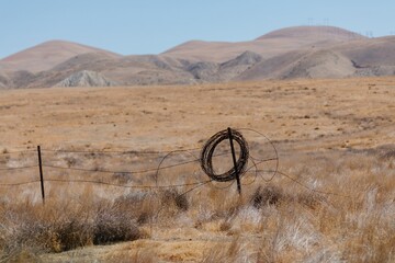 Barbed wire hangs on a fence post in a dry, grassy field in  Carrizo Plain National Monument,...