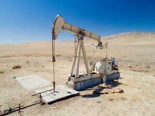A Lufkin pumpjack extracts crude oil in a dry, arid landscape in Mckittrick, California, USA. The oil well pump is used to artificially lift liquid from a well when there isn't enough pressure.