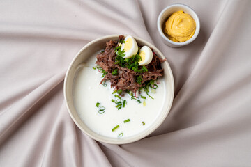 A beautifully arranged bowl features a rich, creamy soup base topped with tender shredded beef and vibrant green chives. Accompanying this dish is a small bowl of mustard, adding a zesty touch