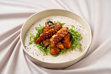 Tender pieces of grilled octopus sit atop a bed of vibrant greens, accompanied by a creamy sauce. The dish showcases vibrant colors and textures, perfect for a gourmet dining experience