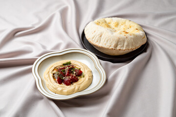 A beautifully arranged dish showcases creamy hummus topped with fresh herbs and vibrant tomatoes, accompanied by warm, fluffy flatbread
