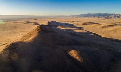Aerial view of a dry riverbed cutting through the arid landscape of Carrizo Plain National Monument in California, USA. Mountains are visible in the distance.